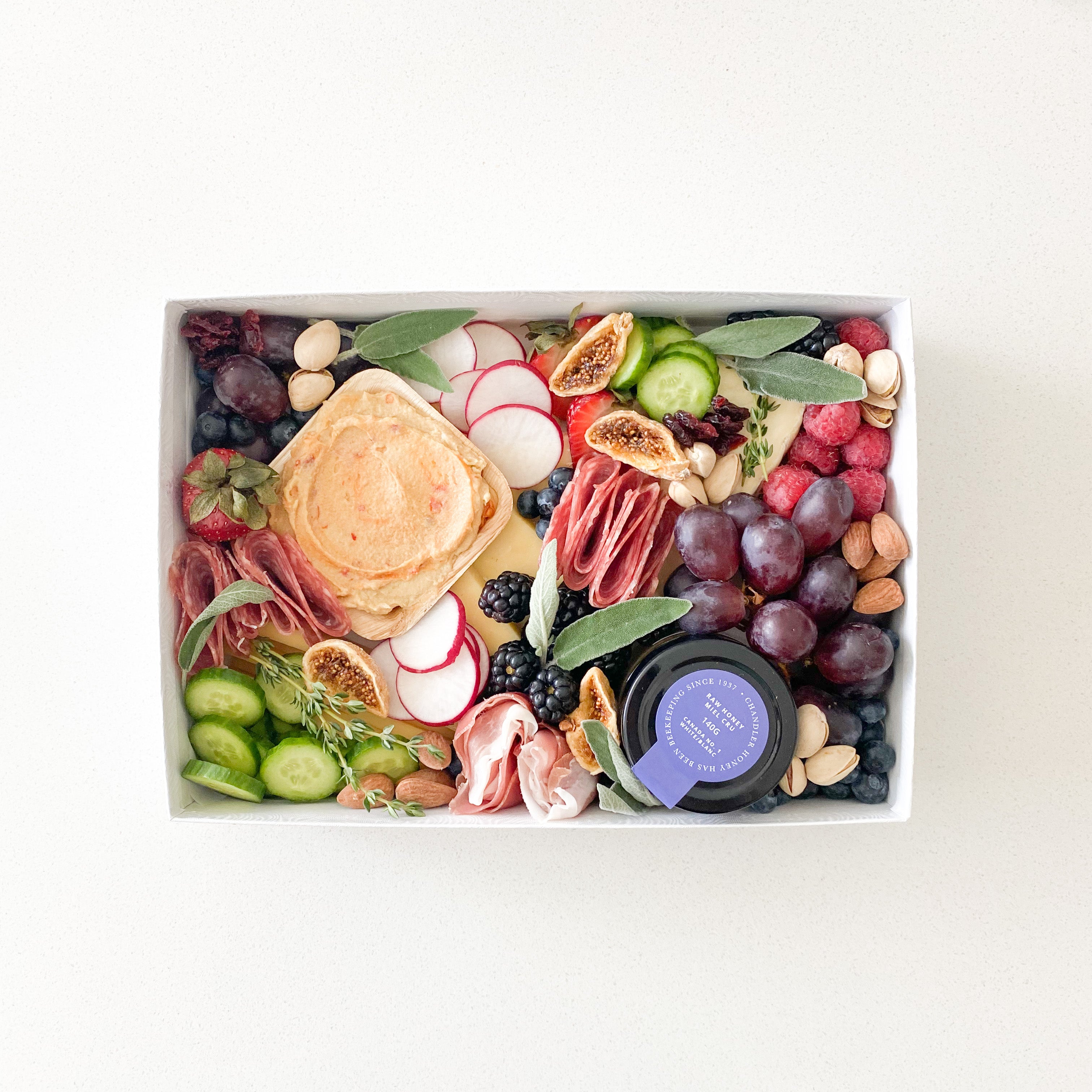 small grazing box with cheese, charcuteries, fruits, vegetables, hummus and creme brulee honey