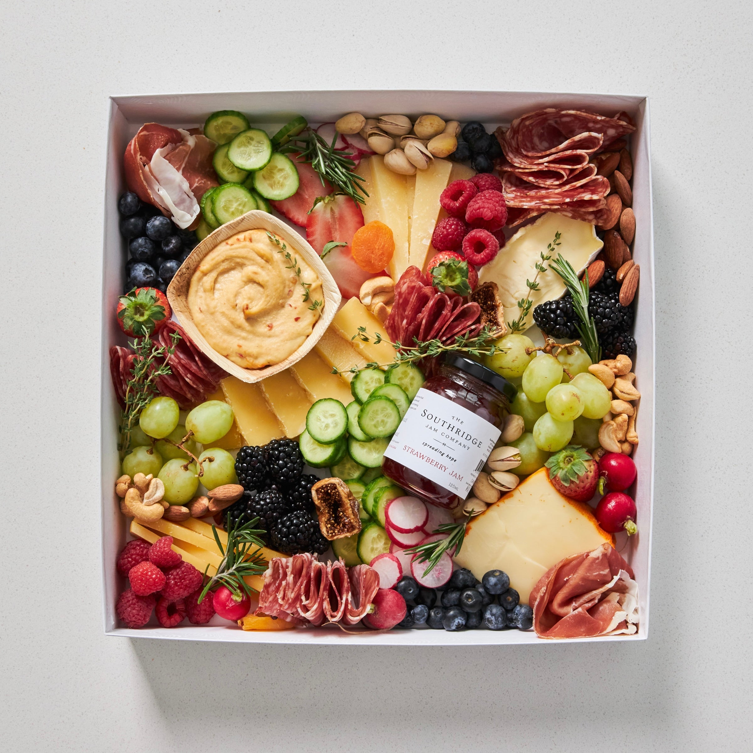 large grazing box with cheese, charcuteries, fruits, vegetables, hummus and jam